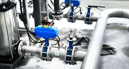 Large industrial water treatment and boiler room. Shiny steel metal pipes and blue pumps and valves.
