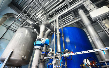 Large industrial water treatment and boiler room. Shiny steel metal pipes and blue pumps and valves.