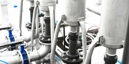 Large industrial water treatment and boiler room. Shiny steel metal pipes and blue pumps and valves.