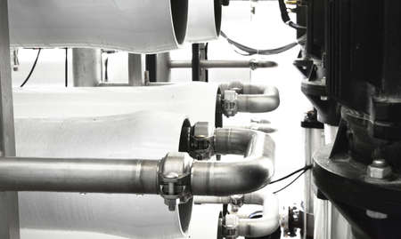 Large industrial water treatment and boiler room. Shiny steel metal pipes and blue pumps and valves.