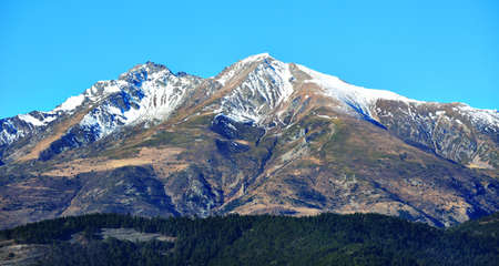 Panoramic view of a French Alps mountaintop with forrest on the bottom against clear blue sky. Parc...