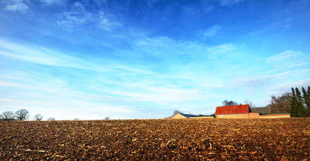 Close-up of a soil prepared for planting with farm buildings in the background. Nature, landscape, alternative lifestyle and production, environmental conservation in Europe. Panoramic viewの写真素材