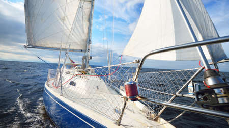 Sloop rigged yacht sailing in an open sea. Top down (high angle) view from a bow with mast and full...