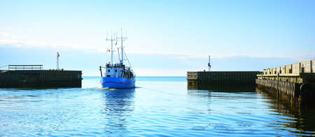 Small ship leaving port on a calm bright day. Clear blue sky. Freight transportation, nautical...
