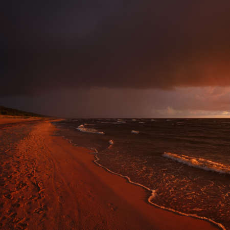 Stormy waves of the Baltic sea under the colorful dramatic sunset clouds. A view from the sandy shore. Epic seascape. Picturesque panoramic scenery. Meteorology, ecology, environmentの写真素材