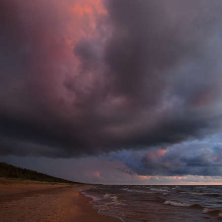 Stormy waves of the Baltic sea under the colorful dramatic sunset clouds. A view from the sandy shore. Epic seascape. Picturesque panoramic scenery. Meteorology, ecology, environmentの写真素材
