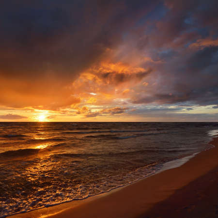 Stormy waves of the Baltic sea under the colorful dramatic sunset clouds. A view from the sandy shore. Epic seascape. Picturesque panoramic scenery. Meteorology, ecology, environmentの写真素材