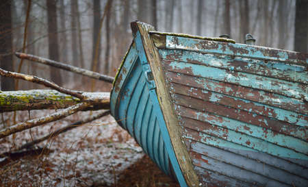 Abandoned old blue wooden boat in a mysterious winter forest. Mossy trees in a white mist. Fresh snow and golden autumn leaves. Concept art, economic decline, recession, philosophy, contrasts, paradoxの写真素材