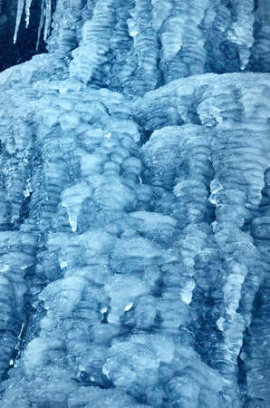 Large blue icicles close-up, cliff in the background. Frozen water, ice texture. Abstract art,...