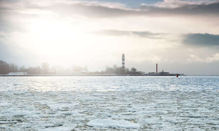 Baltic sea shore at sunset. Lighthouse in the background. Snow, ice fragment on the water. Colorful sunset clouds, golden sunlight. Gulf of Riga, Latvia. Climate change concept. Symbol of hope, peaceの写真素材
