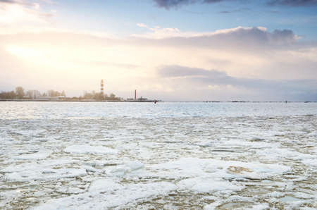 Baltic sea shore at sunset. Lighthouse in the background. Snow, ice fragment on the water. Colorful sunset clouds, golden sunlight. Gulf of Riga, Latvia. Climate change concept. Symbol of hope, peaceの写真素材