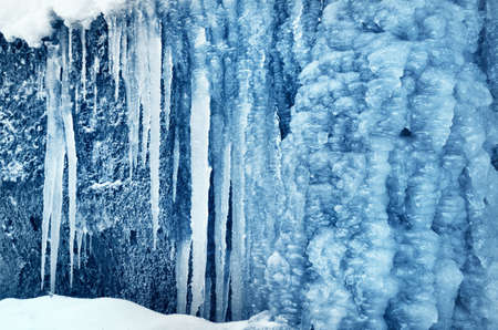 Large blue icicles close-up, cliff in the background. Frozen water, ice texture. Abstract art,...