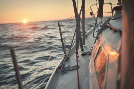 White yacht sailing in the North sea after the storm. Norway. View from the deck to the bow, mast sails. Clear blue sky, soft golden sunset light. Transportation, cruise, recreation, regatta, sportの写真素材