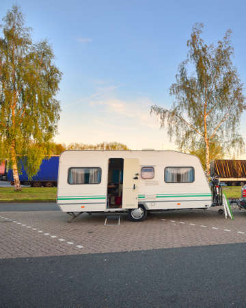 White caravan trailer with a car parked on an asphalt road. Sunny day. Spring landscape. Holland. Lifestyle, freedom, travel, ecotourism, journey, vacations, recreation, transportation, RV, motorhomeの写真素材