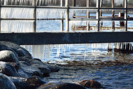 Frozen pier on the rocky shore of the Baltic sea. Clear blue sky. Concept winter landscape. Midday sun. Seasons, ecology, environment, climate change, global warming, anomaly. Panorama, copy spaceの写真素材