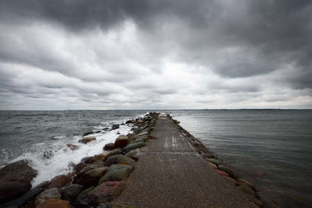 Dark storm clouds above the Baltic sea. Kiel, Germany. Rocks, waves and water splashes close-up. A view from the pier. Fickle weather, climate themes. Nature, tourism, cruise, recreationの写真素材