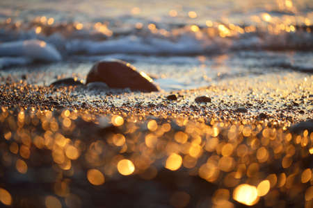 Sea shore at sunset, close-up. Pebbles, storm waves. Abstract background, details blurred in bokeh. Blue, yellow, orange, pink colors. Soft sunlight, golden hour. Peace, meditation, tranquility themesの写真素材
