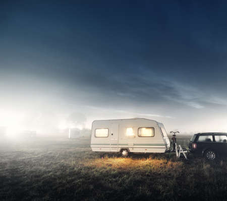 White caravan trailer on a green lawn in a camping site. Twilight sky, moon. Summer landscape. Europe. Wanderlust, travel, tourism, road trip, vacations, recreation, transportation, RV, motorhomeの写真素材