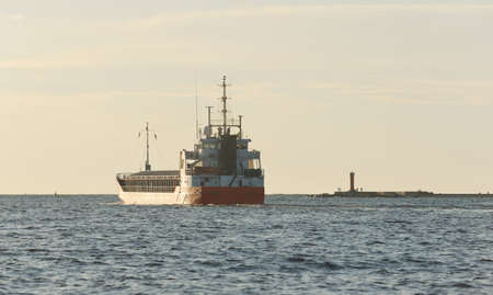 Large red general cargo ship (80 meters length) sailing in an open sea at sunset. Freight transportation, nautical vessel, logistics, global communications, economy, industry, worldwide shippingの写真素材