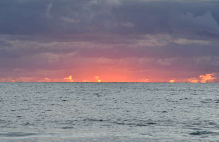 Baltic sea shore at sunset. Soft sunlight, dramatic sky, glowing pink and golden clouds. Waves and...