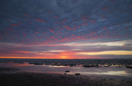 Baltic sea shore at sunset. Soft sunlight, dramatic sky, glowing pink and golden clouds. Waves and...