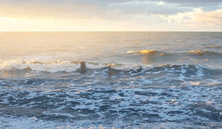 Baltic sea shore at sunset. Soft golden sunlight, dramatic sky, glowing clouds, waves. Idyllic seascape. Travel destinations, ecotourism, nature, weather, climate change. Picturesque panoramic sceneryの写真素材
