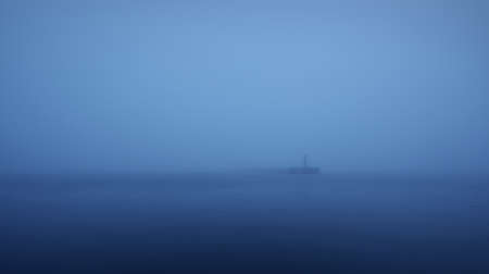 Panoramic view of Baltic sea. Port entrance, lighthouse, breakwaters. Thick fog, mist, blue light. Waves, water splashes, long exposure. Seascape. Monochrome scenery. Danger, safety conceptsの写真素材