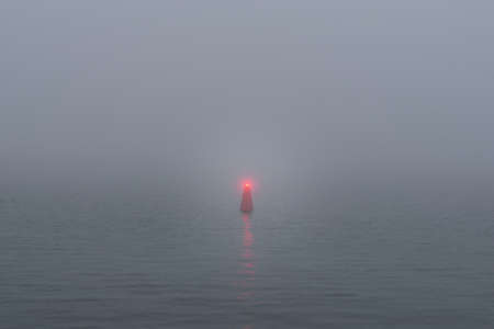 Panoramic view of Baltic sea. Port entrance, lighthouse, red navigational buoy. Thick white fog, mist. Waves, water splashes, long exposure. Seascape. Monochrome scenery. Danger, safety conceptsの写真素材