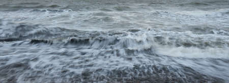 Baltic sea shore at sunset. Soft golden sunlight, dramatic sky, glowing clouds, waves. Idyllic seascape. Travel destinations, ecotourism, nature, weather, climate change. Picturesque panoramic sceneryの写真素材
