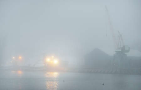 Tugboats and fishing boats (trawlers) moored to a pier in a harbor. Thick white fog. Latvia, Baltic sea. Panoramic view. Service, repair, freight transportation, logistics, industry, commerceの写真素材