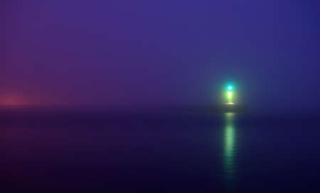Panoramic view of Baltic sea at night. Port entrance, lighthouse, breakwaters. Thick fog, green and blue light. Waves, water splashes, long exposure. Seascape. Monochrome scenery. Danger, safety themeの写真素材