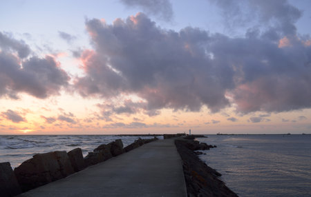 Old pier (walkway, promenade) to the lighthouse. Breakwaters close-up. Clear blue sky, pink sunset clouds, golden sunlight. Seascape, cloudscape. Baltic sea. Spring. Tourism, landmark, navigationの写真素材