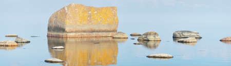 Rocks at the coast of Kasmu (captain's village), Estonia, in a white fog at sunset. Baltic sea. Soft sunlight. Nature, environmental conservation, ecology, ecotourism. Picturesque panoramic sceneryの写真素材