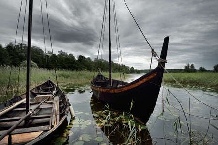 Wooden sailing boats moored to a pier. Birka, BjÃ¶rkÃ¶ island, lake MÃ¤laren, Sweden. Atmospheric landscape. Travel destinations, landmarks, sightseeing, history, historical reenactment, viking ageの写真素材