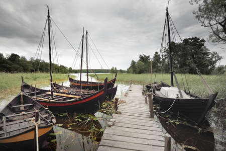 Wooden sailing boats moored to a pier. Birka, BjÃ¶rkÃ¶ island, lake MÃ¤laren, Sweden. Atmospheric landscape. Travel destinations, landmarks, sightseeing, history, historical reenactment, viking ageの写真素材