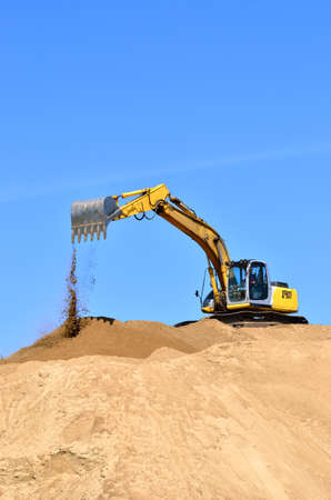 Modern yellow excavator working in a sand quarry, close-up. Clear blue sky. Panoramic view....