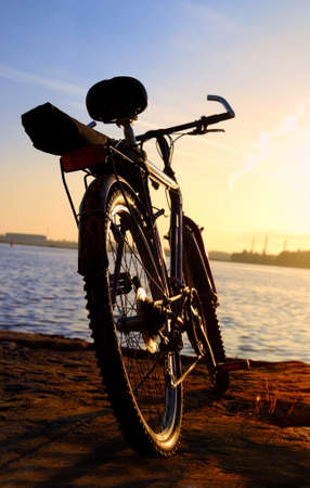 Bicycle silhouette against colorful sunset and industrial port background