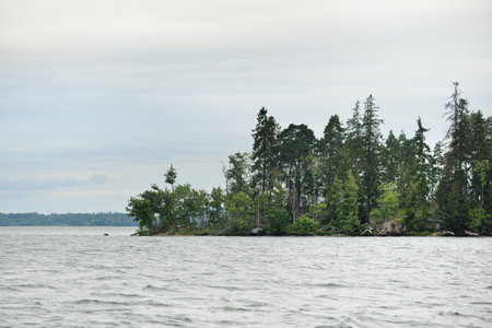 Sailing in MÃ¤laren lake, Sweden. Rocky shore, forest. Dramatic sky after the storm, dark clouds. Nature, environment, travel destinations, ecotourism, hiking, vacationsの写真素材