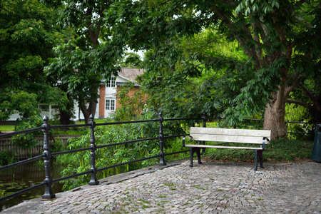 Wooden bench near the canal. Traditional swedish house in the background. Green summer park....