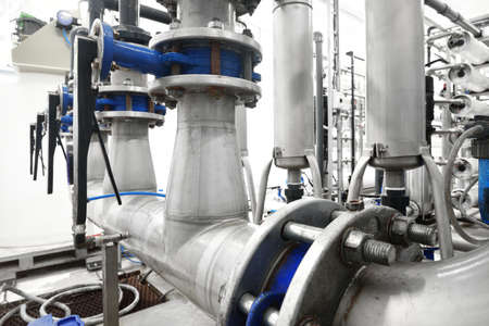 Large industrial water treatment and boiler room. Shiny steel metal pipes and blue pupms and valves.