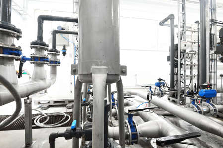 Large industrial water treatment and boiler room. Shiny steel metal pipes and blue pupms and valves.