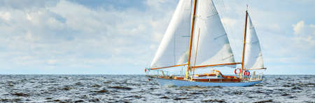 Old expensive vintage wooden sailboat (yawl) close-up, sailing in an open sea. Dramatic cloudscape....