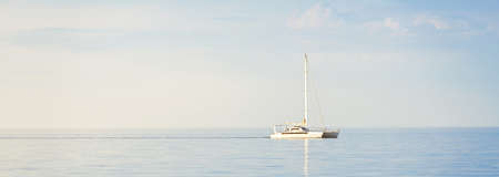 White modern yacht (catamaran) sailing in an open Caribbean sea at sunset. Clear blue sky, symmetry reflections in the water. Idyllic seascape. Travel destinations, sport, leisure activity, recreationの写真素材