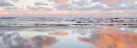 Panoramic view of the Baltic sea from a sandy shore. Clear sunset sky, colorful glowing pink clouds,...