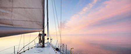 White yacht sailing in an open sea at sunset. Close-up view from the deck to the bow. Clear blue sky...