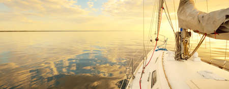 White yacht sailing in the Baltic at sunset. View from the deck to the bow. Glowing clouds,...
