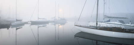 Sailing boats moored to a pier in a thick white morning fog at sunrise, close-up. Yacht club in Kiel, Germany. Sport, recreation, transportation themeの写真素材