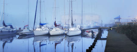 Sailing boats moored to a pier in a thick white morning fog at sunrise, close-up. Yacht club in Kiel, Germany. Sport, recreation, transportation themeの写真素材