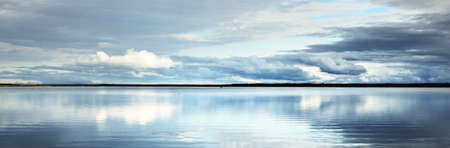 Forest lake with symmetry reflections in crystal clear water, natural mirror. Dramatic sky, ornamental glowing cumulus clouds before the rain. Nature of Scandinavia. Idyllic landscape. Panoramic viewの写真素材