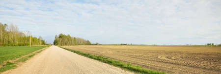 An empty country road through the plowed fields. Dramatic sky. Europe. Transportation, logistics, communications, driving, off-road, remote places. Concept landscape. View from the carの写真素材
